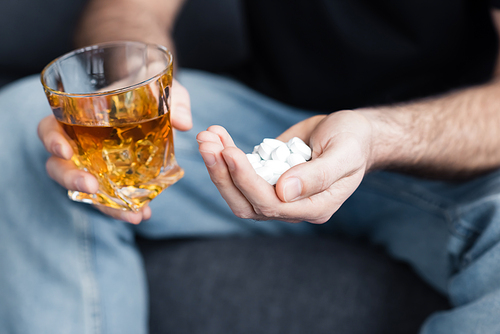 cropped view of sitting man with handful of pills and glass of whiskey