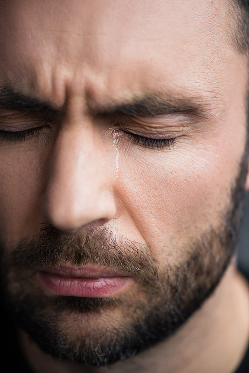 portrait of handsome, bearded depressed man crying with closed eyes