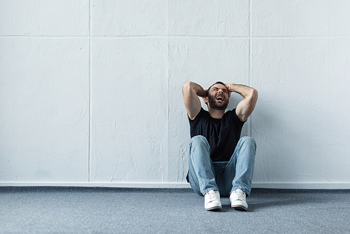 adult depressed man screaming while sitting on floor by white wall