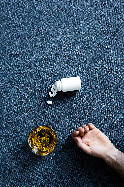 top view of male hand near glass of whiskey and container with pills on grey floor