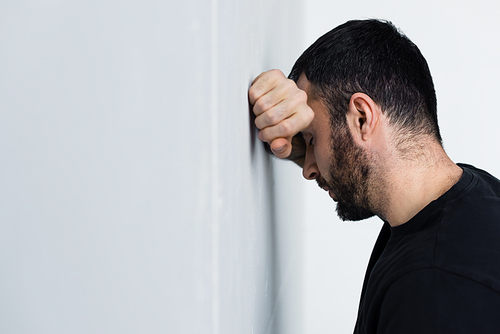depressed unshaven man standing near white wall with closed eyes