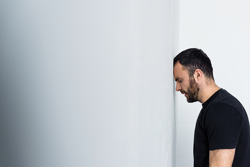 handsome depressed man standing by white wall with closed eyes