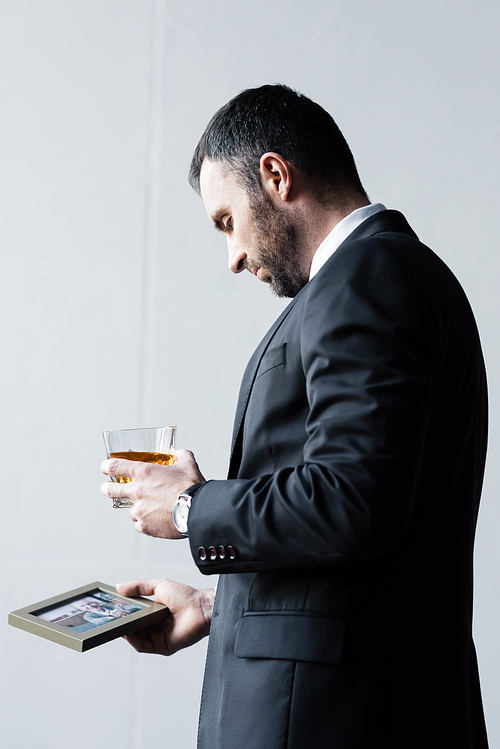 upset bearded man in suit holding photo in frame and glass of whiskey