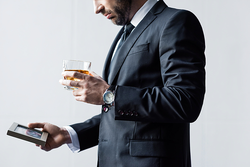 partial view of man in suit holding glass of whiskey and photo in frame