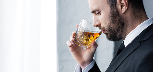panoramic shot of sad, handsome bearded man drinking whiskey
