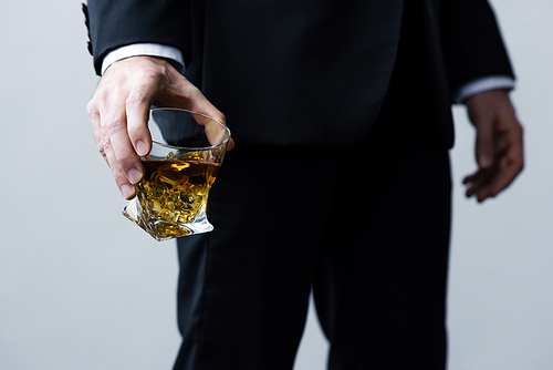 cropped view of adult man in black suit holding glass of whiskey