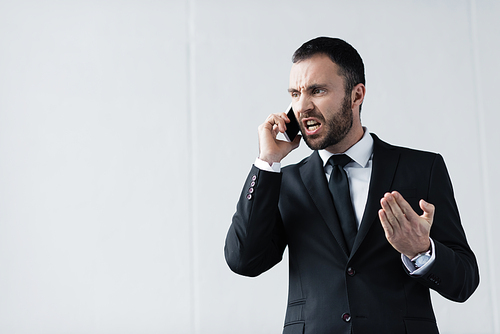 angry businessman in black suit quarreling while talking on smartphone