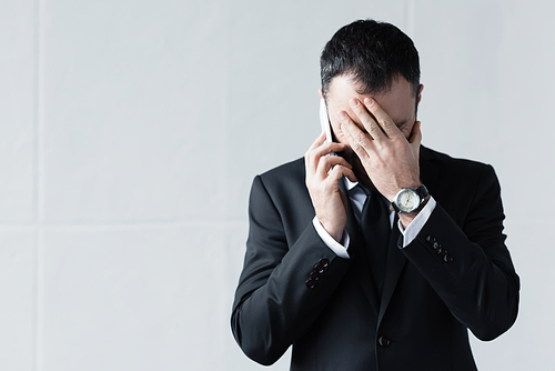 disappointed man in black suit using smartphone and holding hand on face
