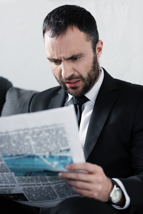 selective focus of shocked bearded businessman reading newspaper