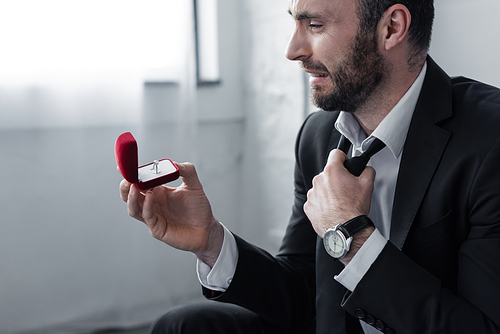 depressed bearded man crying while looking at gift box with ring