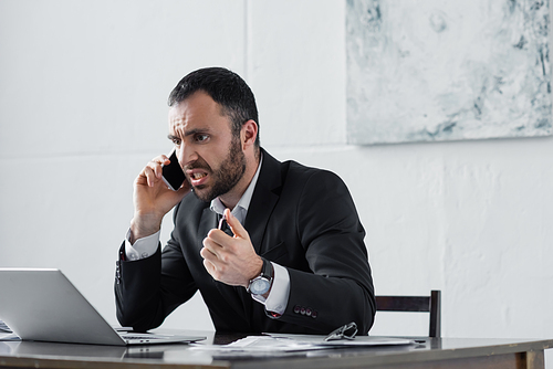 angry businessman yelling while sitting at workplace and talking on smartphone