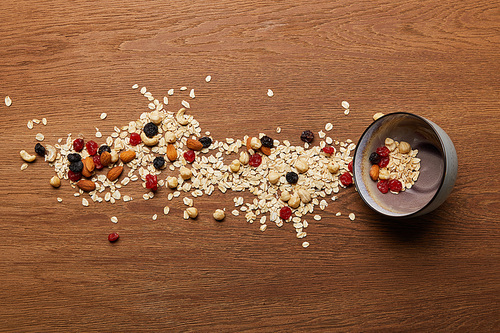 top view of oat flakes scattered with nuts and dried berries near bowl at wooden table