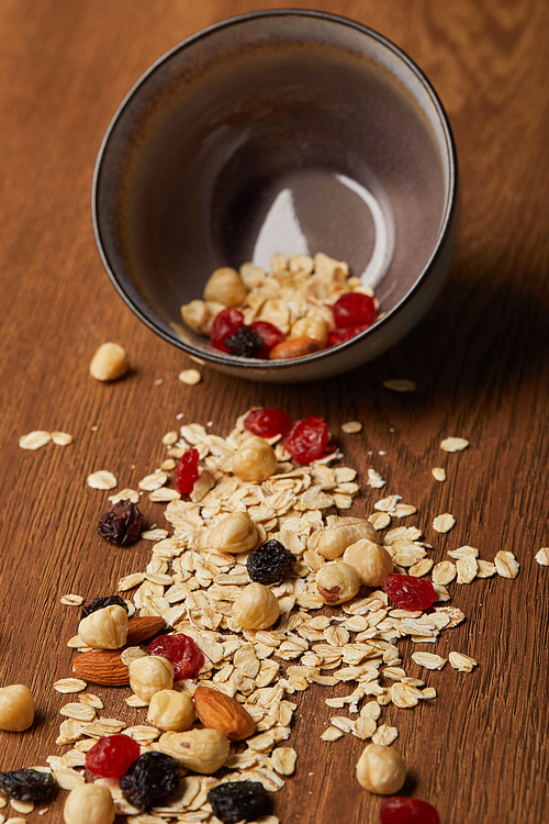 oat flakes scattered with nuts and dried berries from bowl on wooden table
