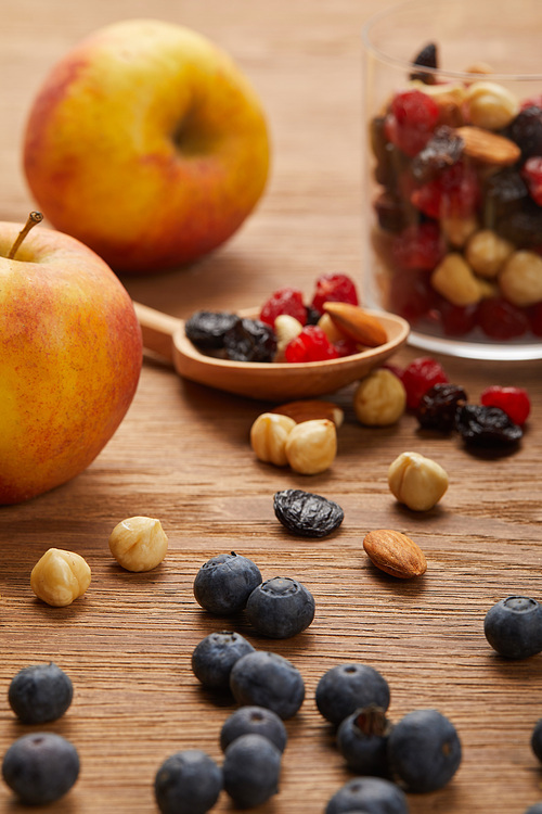close up of blueberries and hazelnuts near apples and spoon on wooden table