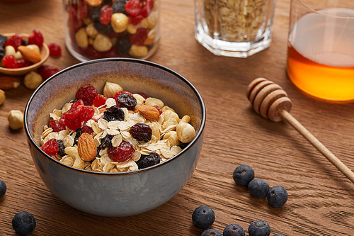 selective focus of cereal in bowl with nuts and dried berries prepared for breakfast on wooden table