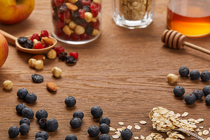 selective focus of oat flakes, nuts, honey and berries on wooden table with copy space