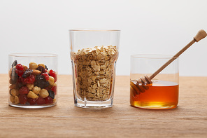 glasses with dried berries, nuts, oat flakes and honey on wooden table isolated on grey