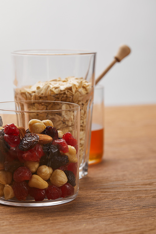 glasses with dried berries, nuts, oat flakes on wooden table isolated on grey