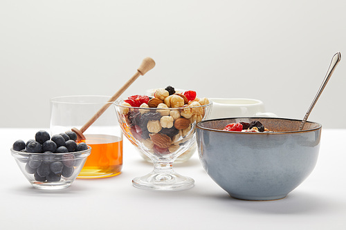 bowls and glasses with berries, nuts, honey and cereal served for breakfast on white table isolated on grey
