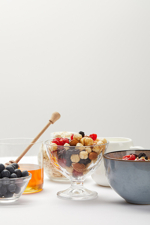 bowls with berries, nuts, honey and cereal served for breakfast on white table isolated on grey