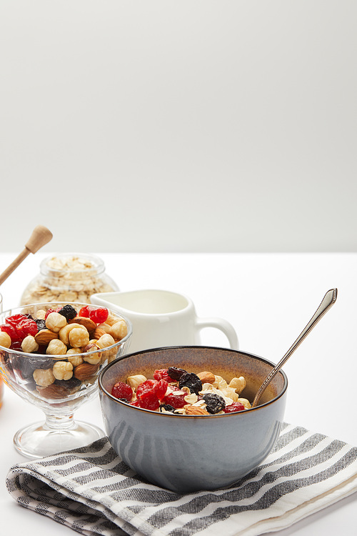 bowls with berries, nuts, honey and oat flakes served for breakfast on white table isolated on grey