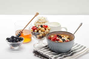 muesli with berries, nuts and honey for breakfast on white table isolated on grey