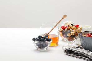 muesli with berries, nuts and honey served for breakfast on white table isolated on grey