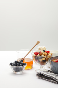 muesli with berries, nuts and honey in bowls served for breakfast on white table isolated on grey