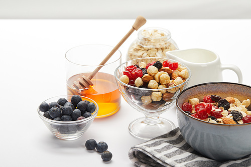 muesli with berries, nuts and honey in bowls served for nutritious breakfast on white table isolated on grey