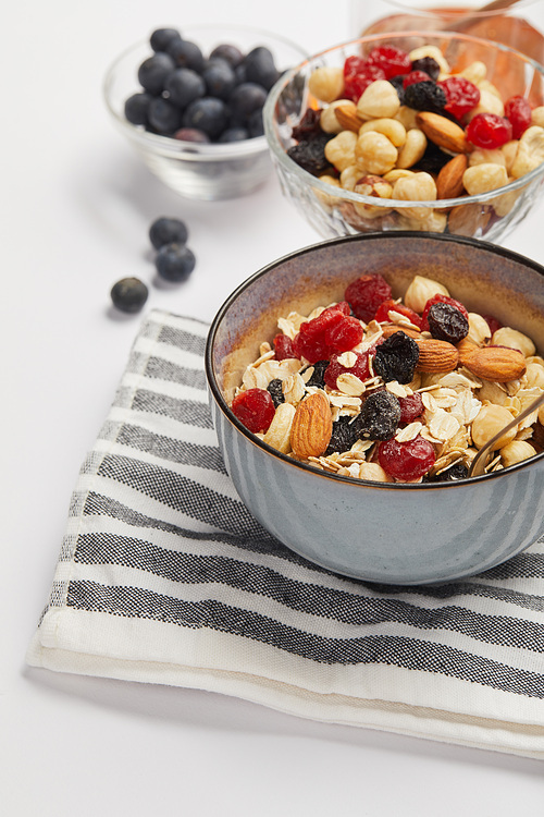 bowl on striped napkin with oat flakes, nuts and berries on white table