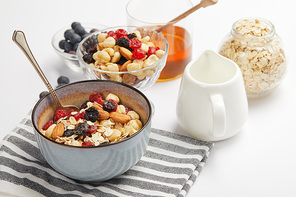 bowl on striped napkin with oat flakes, nuts and berries on white table with milk jug