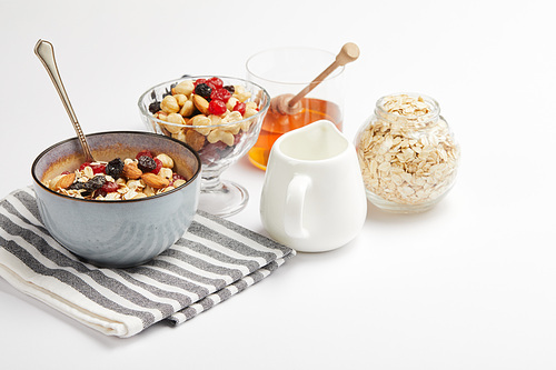 bowl on striped napkin with oat flakes, nuts and berries on white table with copy space