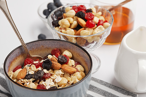 close up of bowl on striped napkin with oat flakes, nuts and berries on white table