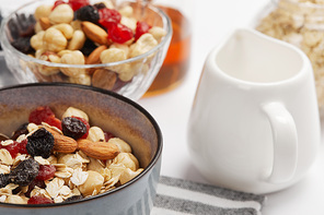 selective focus of bowl on striped napkin with oat flakes, nuts and berries near milk jug