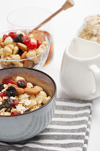 selective focus of bowl on striped napkin with oat flakes, nuts and berries near white milk jug