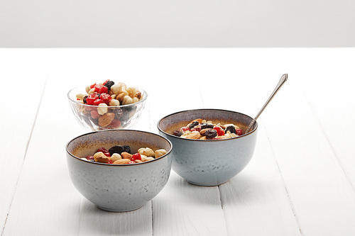 bowls with muesli, dried berries and nuts served for breakfast on white table isolated on grey