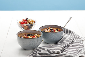 bowls with muesli, dried berries and nuts served for breakfast near striped napkin isolated on blue