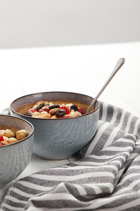 bowls with muesli, dried berries and nuts served for breakfast near striped cloth isolated on grey