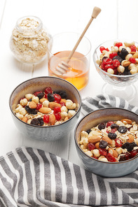 bowls with muesli, dried berries and nuts served for breakfast with honey on white wooden table