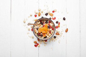 top view of bowl full of muesli with dried apricots, berries and scattered nuts around on white wooden table
