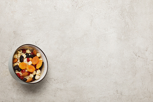 top view of bowl with muesli, dried apricots and berries, nuts on textured grey surface