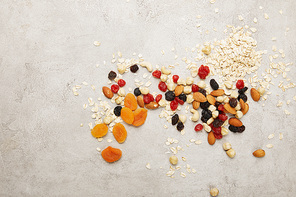 top view of oat flakes, dried apricots and berries, nuts messy scattered on textured grey surface table