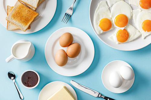top view of table setting for breakfast with toasts and fried eggs on blue background