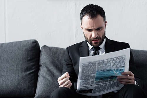 bearded worried businessman reading newspaper while sitting on sofa