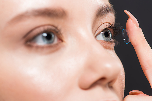 selective focus of woman attaching contact lens isolated on black