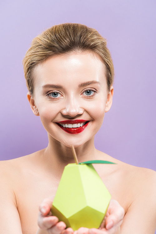 selective focus of happy naked young woman holding decorative green ripe pear isolated on purple