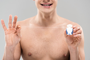 cropped view of naked young man holding dental floss isolated on grey