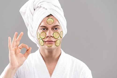 front view of man with cut cucumbers on face showing okay sign isolated on grey