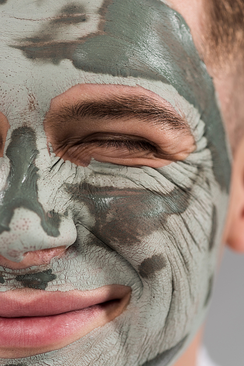 cropped view of smiling young man with clay mask with closed eye