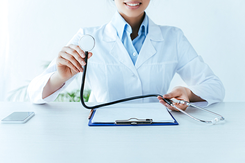 cropped shot of young latin doctor holding stethoscope while sitting at workplace